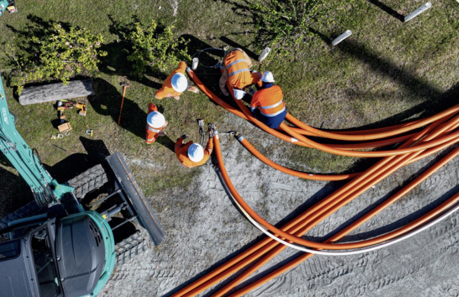 Crew laying underground utility conduits alongside an excavator on a Brisbane site